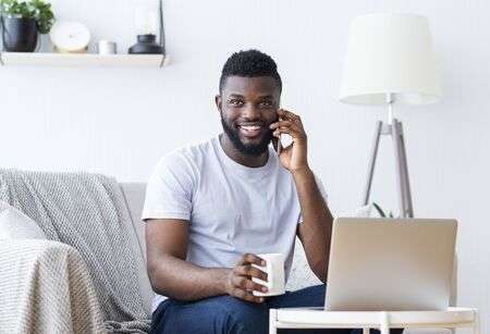 139833990-home-office-positive-african-guy-working-on-laptop-and-calling-on-phone-free-space.jpg